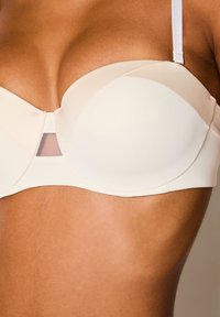 Reggiseno color crema con coppe sagomate, texture morbida e un accento in rete trasparente tra le coppe, dotato di spalline regolabili per una vestibilità perfetta.