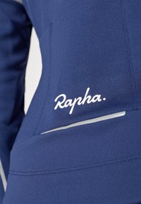 Pomorska biciklistička majica s glatkom teksturom, s bijelim logotipom "Rapha" i reflektirajućom trakicom za vidljivost. Dizajnirana za performanse.