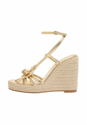Arany színű ék sarkú szandál bokapánttal, nyitott orral, elöl virág díszítéssel és fonott juta talppal.