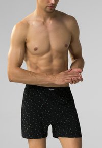 Czarne bokserki z zielonym wzorem liści, wykonane z miękkiego materiału. Posiadają elastyczny pas z logo oraz zapięcie na guziki z przodu.