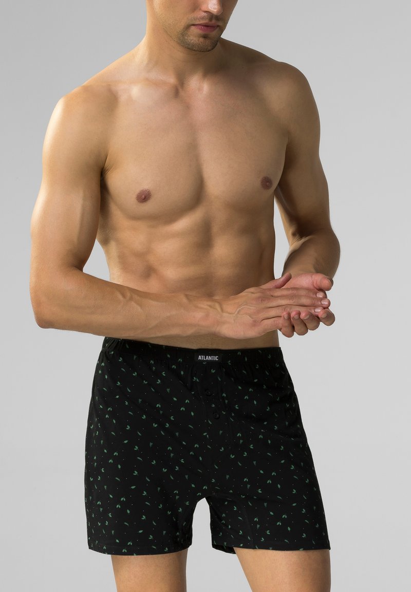 Czarne bokserki z zielonym wzorem liści, wykonane z miękkiego materiału. Posiadają elastyczny pas z logo oraz zapięcie na guziki z przodu.