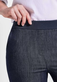 Pantalon en denim foncé avec une taille côtelée bleu marine, présentant une texture lisse et des détails de couture subtils le long des poches.