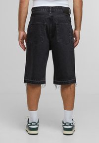 Sorte denimshorts med frynset kant, to baklommer og en lærrem, iført hvite sokker og grønne Nike sneakers.