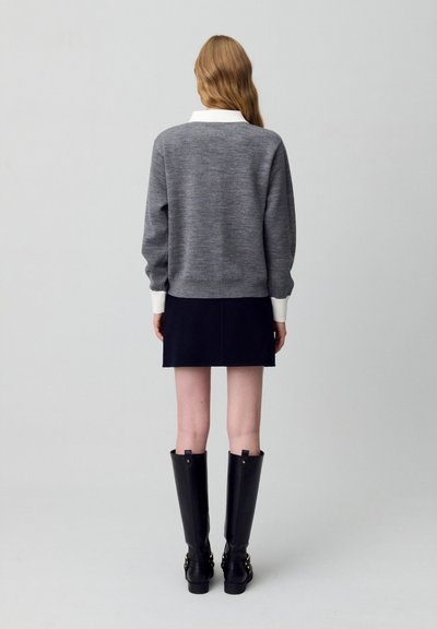 Maglione grigio con colletto bianco, gonna blu navy e stivali neri al ginocchio; attenzione alla texture e al design stratificato.