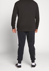 Czarna bluza z długimi rękawami, zestawiona z granatowymi spodniami dresowymi z białymi bocznymi panelami i napisem. Materiał wydaje się miękki, o luźnym kroju.