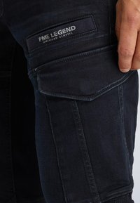 Donkerdenim cargoshorts met een patch pocket met het label "PME LEGEND AMERICAN CLASSIC", zichtbare stiksels en een gladde textuur.