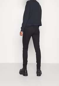 Černé elastické kalhoty s úzkým střihem, elegantního designu, s bočními a zadními kapsami, spojené s volným tmavým topem s dlouhým rukávem.