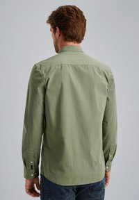 Camicetta verde in cotone a maniche lunghe con colletto button-down, dettagli di cucitura visibili e bottoni ai polsini; la vista posteriore mostra una texture liscia.