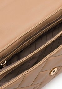 Interno di una borsa a spalla in pelle beige con tasche con zip, texture liscia e dettagli in oro. Fodera trapuntata con motivo diagonale.