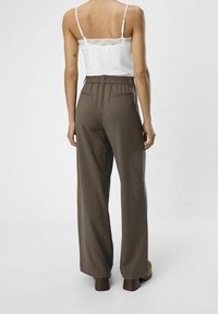 Hnědé široké kalhoty s elastickým pasem a bočními kapsami, doplněné bílým topem s krajkovou vsadkou. Hladká textura.