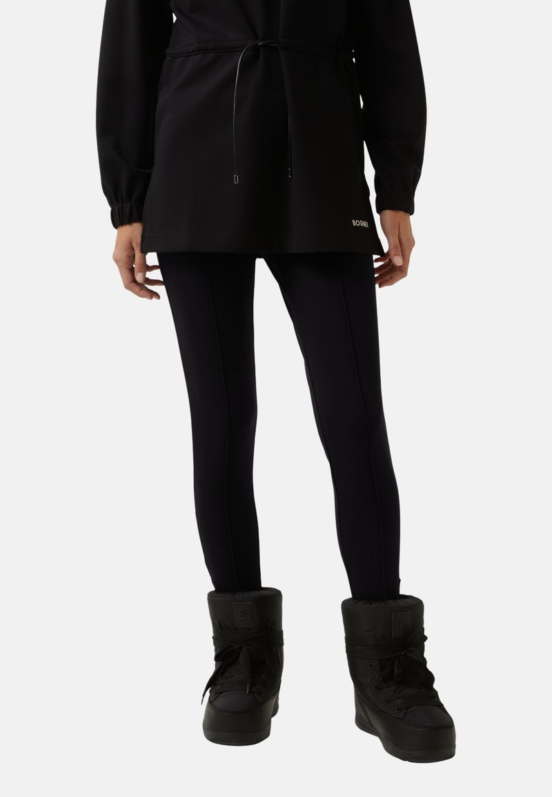 Zwarte sweatshirt met een koord in de taille, gecombineerd met strakke zwarte leggings en zwarte, geïsoleerde sneeuwlaarzen met bontvoering.