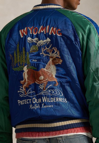 Modra in zelena bomber jakna z vezenim motivom divjih živali, napisoma "WYOMING" in "ZAŠČITIMO NAŠO DIVJINO", s prešito teksturo in rebrastim robom.