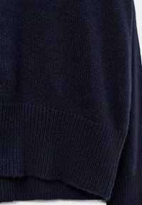 Mornarji modra pletena pulover s prepletenim robom, mehkega tekočin in rahlo ohlapnega kroja. Tkanina prikazuje fino šivano vzorčenje.