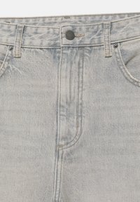 Jean en denim gris clair au niveau de la taille avec fermeture par bouton, passants pour ceinture, poches avant et détails de couture visibles.