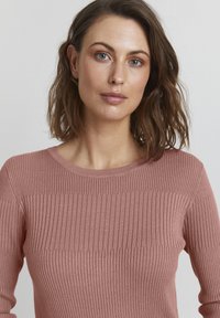 Różowy sweter z prążkowanego dzianiny z okrągłym dekoltem i fakturowanym wzorem, z poziomymi i pionowymi prążkami.