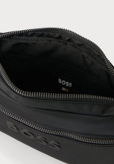 Pochette noire zippée avec logo BOSS embossé et ouverture supérieure montrant un intérieur en tissu noir avec une petite étiquette BOSS à l'intérieur.