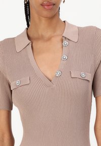 Strikket kjole i taupe med V-hals, korte ermer og dekorative knapper med blomstermønster. Ribbet tekstur med en tettsittende silhuett.