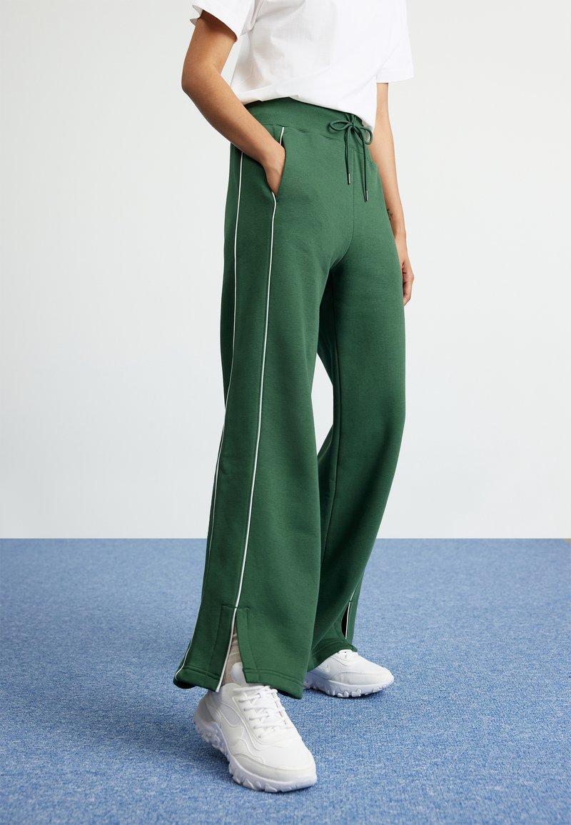 Gröna vida sweatpants i mjukt tyg, med vit sidopiping, elastisk midja med dragsko, och sidofickor.