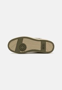 Green and beige sneaker sole features a zigzag tread pattern, circular accent, and brand logo. Rubber material with textured detailing.