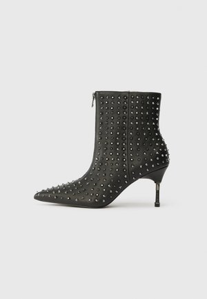 Botas de tornozelo em couro preto com bicos pontiagudos, decoradas com tachas prateadas e detalhes em forma de estrela, apresentando um salto de altura média e fecho lateral.