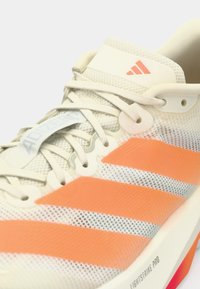 Leichter Laufschuh mit einem Mesh-Obermaterial in Weiß und orangenen Streifen, ausgestattet mit einer gepolsterten Sohle und auffälligem Branding auf der Zunge.