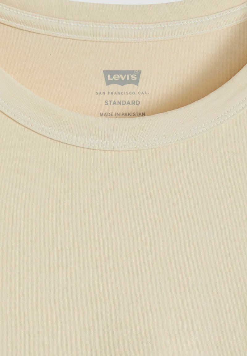 Colletto di una T-shirt Levi's color crema con etichetta stampata che recita "Levi's, San Francisco, CAL., Standard, Made in Pakistan."