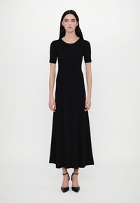 Abito nero a costine con maniche corte, corpetto aderente e orlo svasato. Realizzato in materiale a maglia con una texture liscia. Abbinato a tacchi neri.