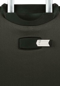 Maleta negra con ruedas y tela texturizada, con asa retráctil y ranura para etiqueta de equipaje con información personal.