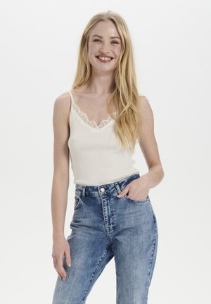 Top a canotta a coste color crema con pizzo, abbinato a jeans blu chiari a vita alta. La canotta ha spalline sottili e un design aderente.