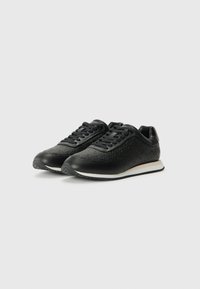 Svarte sneakers med en teksturert overdel med et sirkulært mønster, flate lisser og en hvit såle. Rund tå og polstret ankelstøtte.