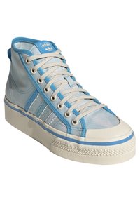 Korkeat tennarit vaaleansinisestä verkosta, jossa on beige kumiulkopohja, siniset yksityiskohdat ja klassinen kolmiraitasuunnittelu sivulla.