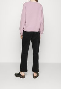 Pull en maille rose clair avec ourlet côtelé, associé à un pantalon large noir. Chaussures : sabots noirs ornés de clous argentés et semelle en bois.