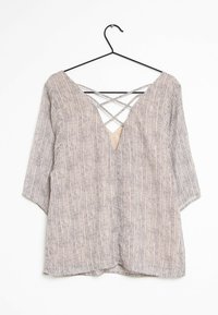 Blusa leggera a fantasia con scollatura a V profonda e dettaglio incrociato sulla schiena. Il colore è beige con piccoli puntini neri. Maniche a tre quarti.