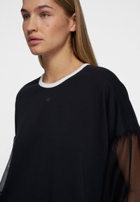 Zwarte sweatshirt met een ronde witte halslijn, voorzien van doorschijnende zwarte stofaccenten bij de mouwen. Eenvoudig, minimalistisch ontwerp.