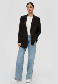 Černý dvouřadý blazer se strukturovaným designem, kombinovaný s světle modrými širokými džíny a bílými platformovými teniskami. Hladký povrch látky.