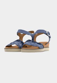 Sandales ouvertes bleues avec brides tressées, fermeture à boucle à la cheville, talon compensé en liège et semelle beige striée sur fond blanc.