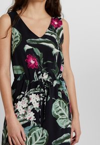 Vestido floral con cuello en V, tiene un fondo negro, grandes hojas verdes, flores rosas y blancas, y una cintura con cordón ajustable. Tela suave.