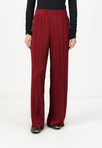 Maroon pleated wide-leg pants with a stretchy waistband. Features vertical texture and a smooth finish. Worn with printed animal-pattern shoes.