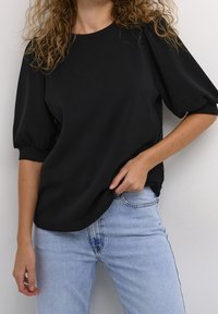 Svart topp med puffärmar i mjukt material, med rund halsringning och avslappnad passform, kombinerad med ljusblå denimjeans.