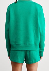Conjunto de sudadera verde y pantalones cortos confeccionado con tela suave. Diseño casual con un ajuste relajado y detalles de dobladillo acanalado.