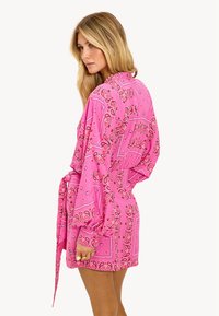 Robe portefeuille à manches longues avec imprimé bandana rose, ceinturée à la taille et coupe décontractée. Le tissu présente une texture lisse et des couleurs vives.