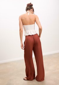 Witte smockpeplumtop gecombineerd met losse, roestkleurige wijde broek. Glad materiaal met een lichte glans, minimalistisch ontwerp en geen zichtbare patronen.