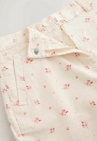 Pantalon de couleur crème avec imprimé floral rose, poche avant, fermeture éclair et détail de fermeture à crochet et barre.