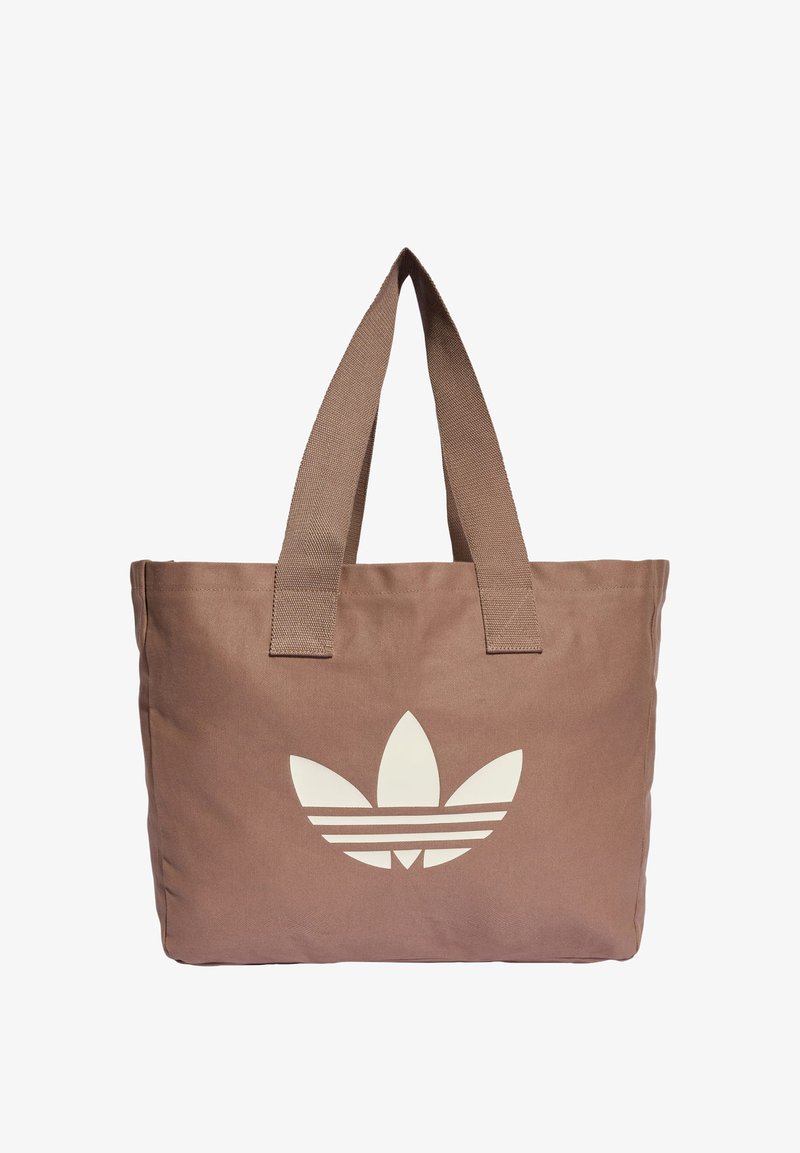 Καφέ υφασμάτινη τσάντα tote με φαρδιές λαβές και μεγάλο λευκό λογότυπο trefoil της Adidas στο κέντρο της μπροστινής πλευράς.