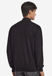 Czarny sweter typu pulower wykonany z miękkiego materiału, z kołnierzem, długimi rękawami i ściągaczami na mankietach. Prosty wzór bez widocznych wzorów.