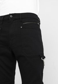 Pantalones cargo negros hechos de tela texturizada, con un bolsillo con cremallera, acentos de metal y un diseño de cintura clásica.