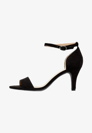 Juodų zomšinių aukštakulnių sandalų su kulkšnies dirželiu, atvira pirštine ir siauru kulnu. Lygus paviršius su minimalistiniu dizainu.