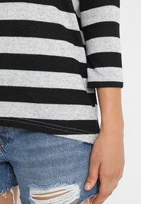 Pasiasty top w czarno-szarym dzianinowym materiale z rękawami o długości trzech ćwierci, w połączeniu z przetartymi szortami dżinsowymi z postrzępionymi krawędziami.