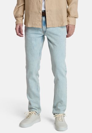 Jasnoniebieskie jeansy z denimu o prostym kroju, z widocznymi przeszyciami i klasycznym designem z pięcioma kieszeniami, zestawione z jasnymi tenisówkami.