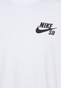 Weißes Baumwoll-T-Shirt mit einem schwarzen "Nike SB" Logo-Graphic auf der linken Seite. Kurzärmlig und mit rundem Ausschnitt. Weicher Stoff.